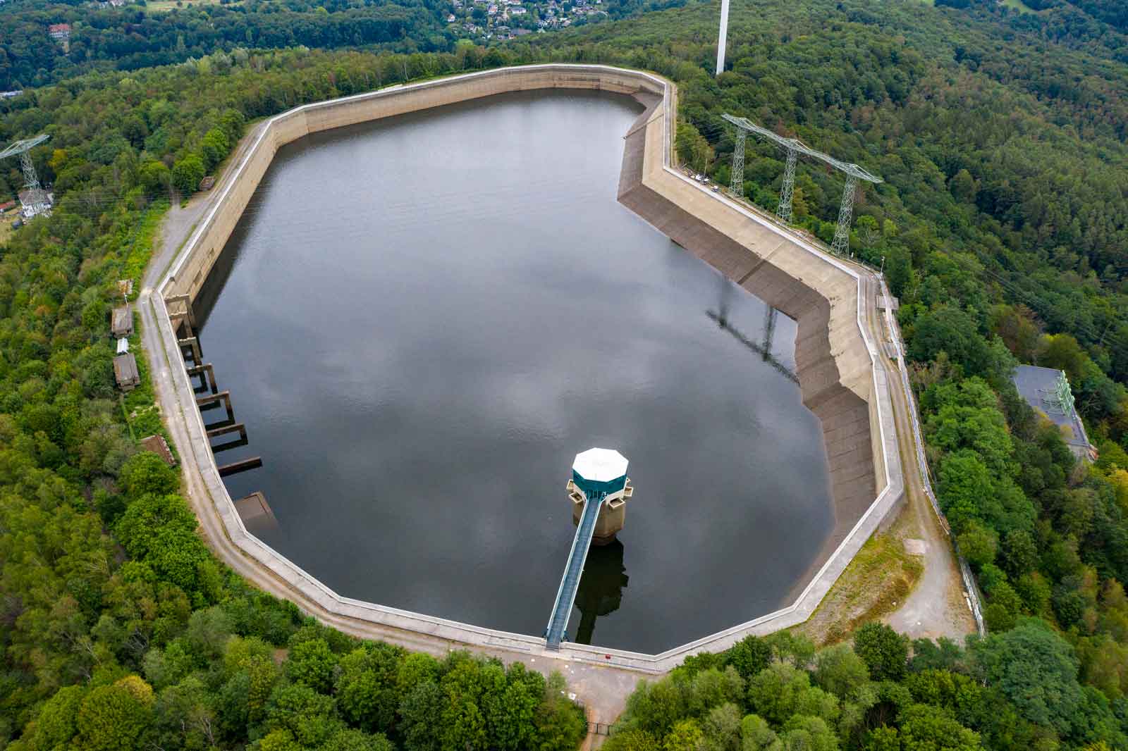 Aerial view of a water reservoir, surrounded by trees and a concrete wall managing the water level.