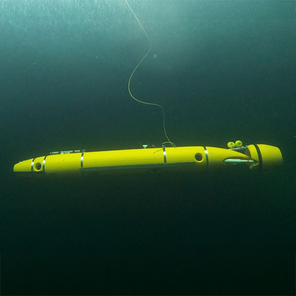 A yellow underwater vehicle floats in deep water, with a long cable leading to the surface.