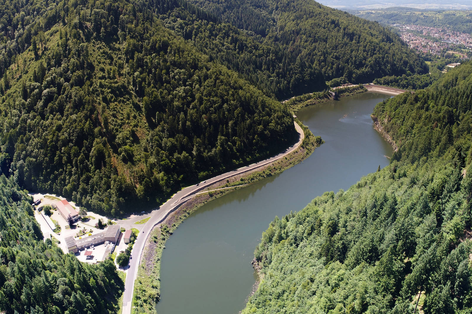 Luftaufnahme einer kurvenreichen Straße entlang eines Flusses, umgeben von dicht bewaldeten Hügeln.