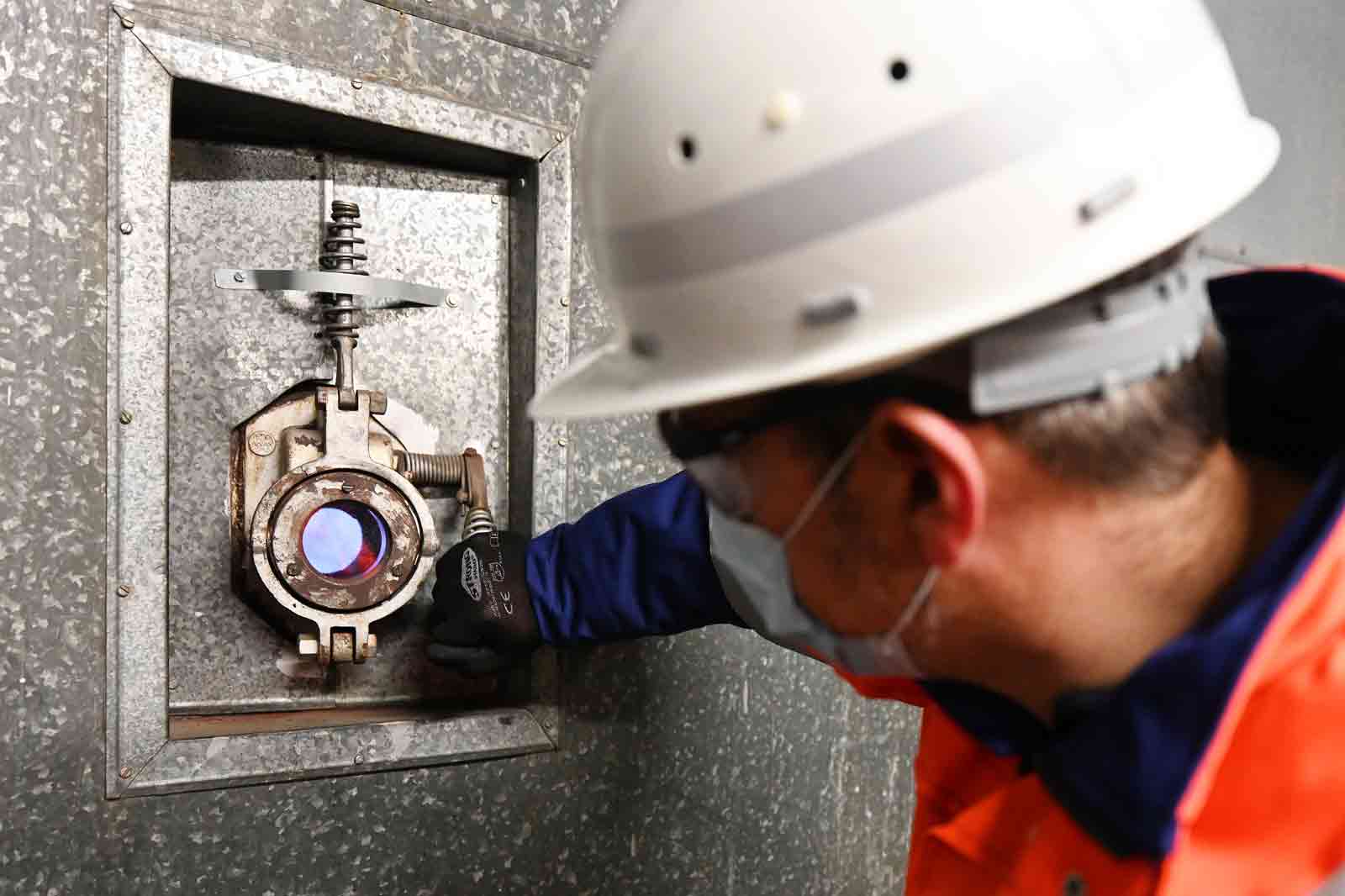 A worker in a hard hat and gloves operates a technical device installed in a metallic wall.