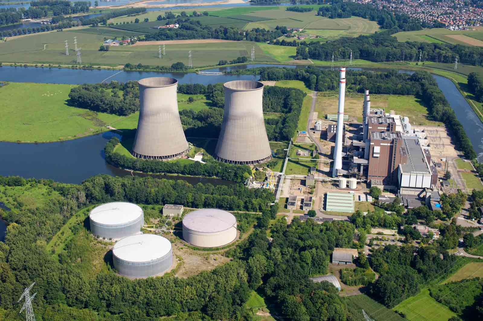 An aerial view of a power plant featuring cooling towers, storage tanks, and surrounding greenery.