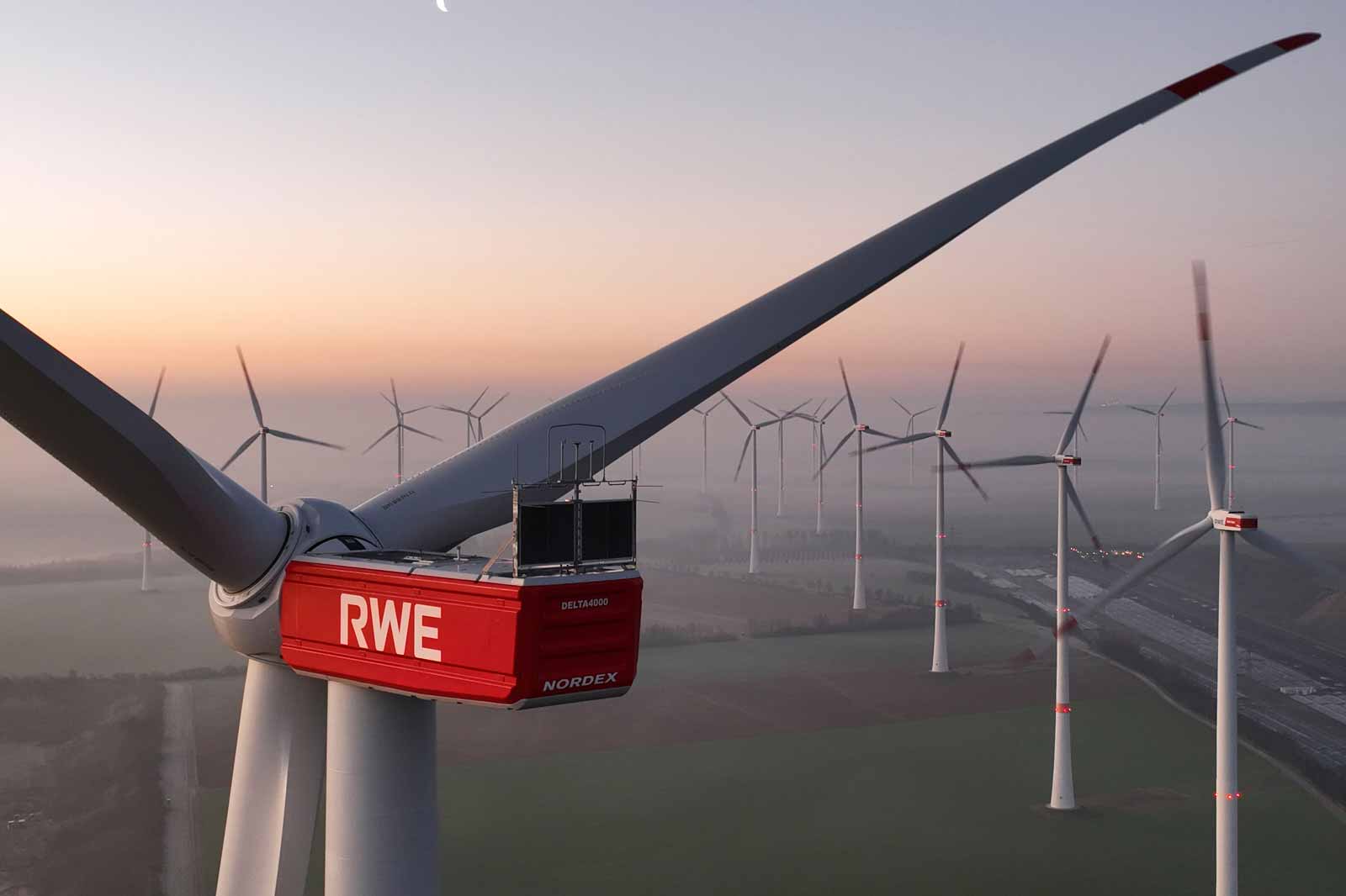 Nahaufnahme eines rot-weißen Windrades mit mehreren Windrädern im Hintergrund bei Sonnenaufgang.