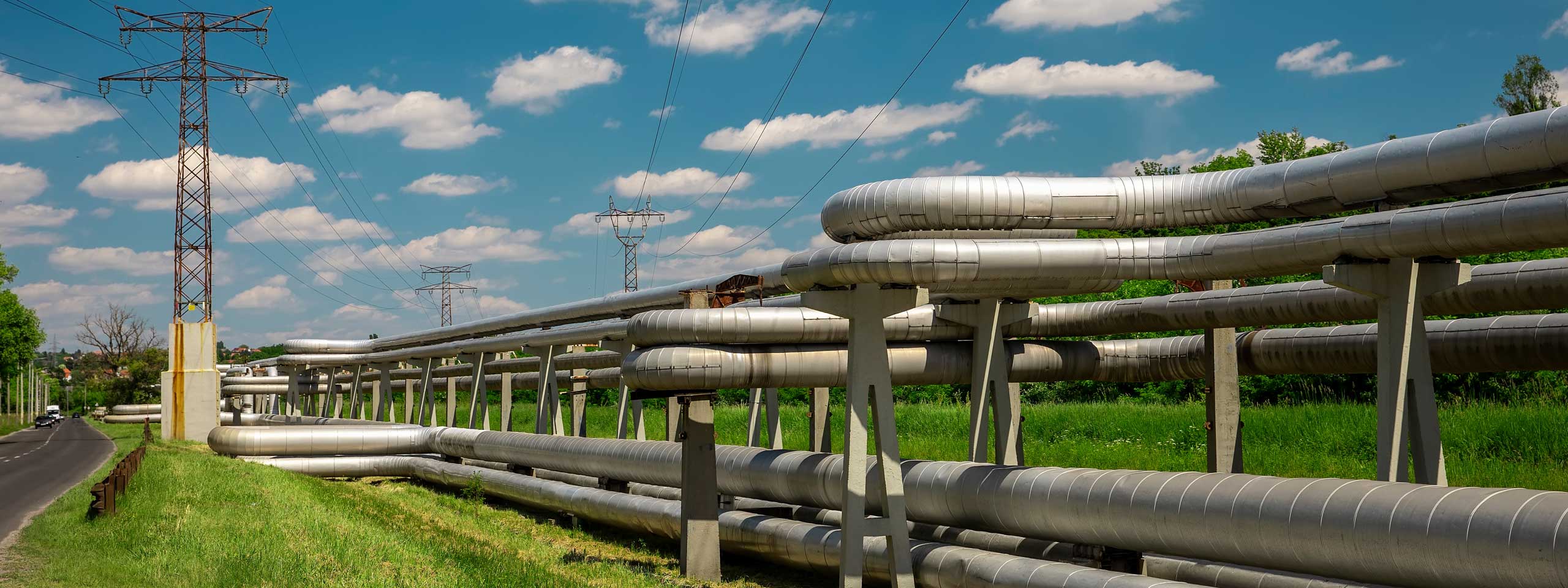 Eine Landschaft mit einer Reihe großer Metallrohre neben einer Straße, umgeben von Stromleitungen und blauem Himmel.
