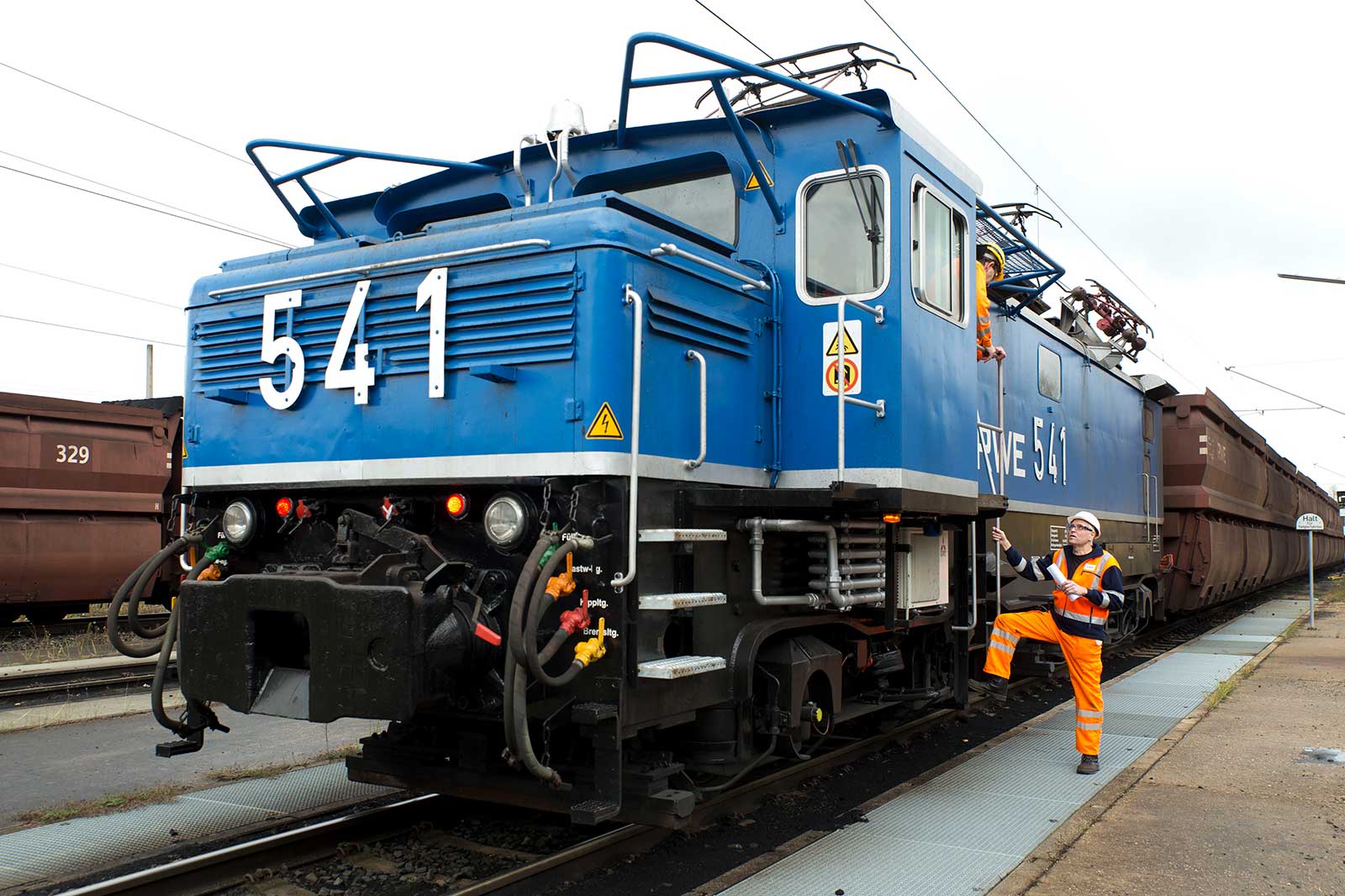 Eine blaue Elektrolokomotive mit der Nummer 541 steht auf den Gleisen. Arbeiter in orangener Sicherheitskleidung kümmern sich um die Lokomotive.