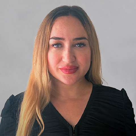 A person with long, blonde hair is wearing a black top against a grey background.
