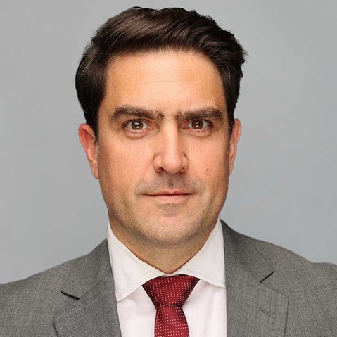 A man in a grey suit and red tie against a neutral background.