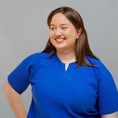 A woman poses confidently in a bright blue top with textured stripes against a grey background.