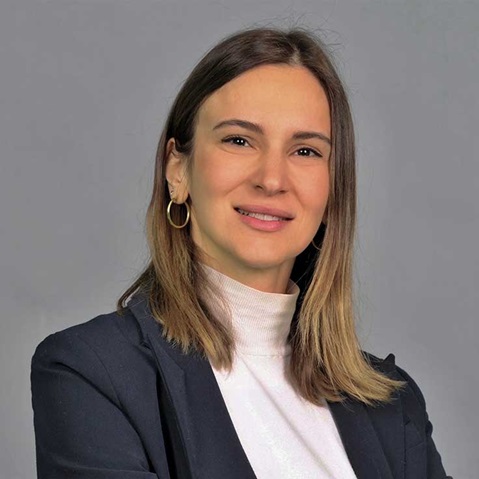 A person is wearing a black blazer and a light jumper. The background is grey.
