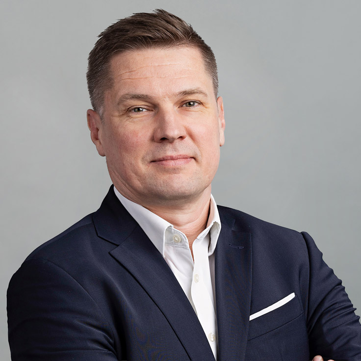 A man in a smart suit stands with crossed arms against a neutral background. Portrait of Thomas Frederiksen.