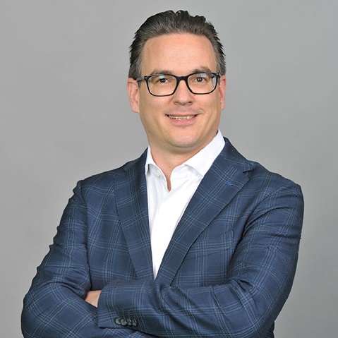 A man in a checked blazer with crossed arms against a grey background.