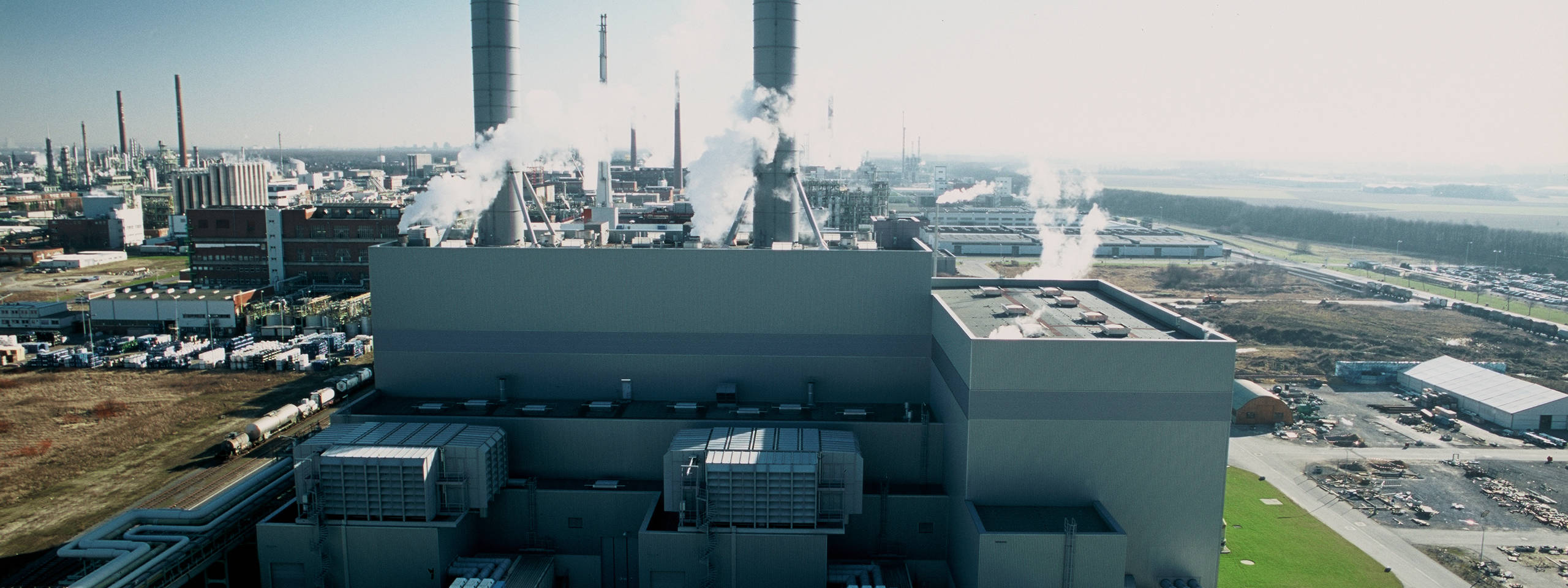 Blick auf ein Industriegebiet mit rauchenden Schornsteinen und einer großen Anlage im Vordergrund.