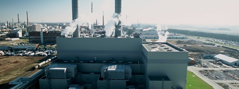 Blick auf ein Industriegebiet mit rauchenden Schornsteinen und einer großen Anlage im Vordergrund.