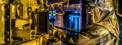 A worker in protective gear operates machinery in an industrial setting with yellow and blue lighting.