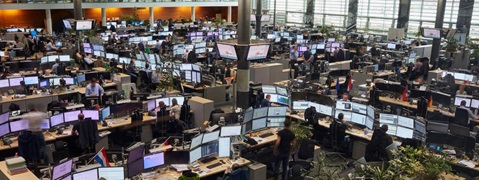 View of a modern office featuring numerous workstations and screens, all occupied by employees.