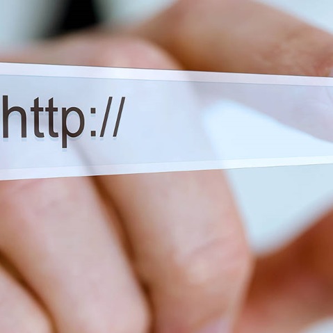 Eine Hand hält eine URL-Leiste mit 'http://' im Fokus, Hintergrund ist unscharf.