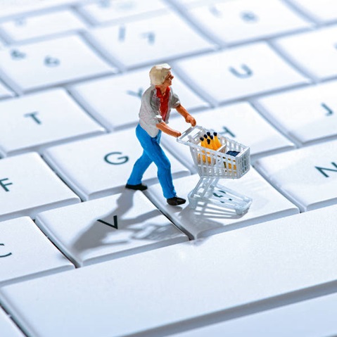 Eine kleine Figur mit einem Einkaufswagen steht auf einer Computertastatur und transportiert Flaschen.