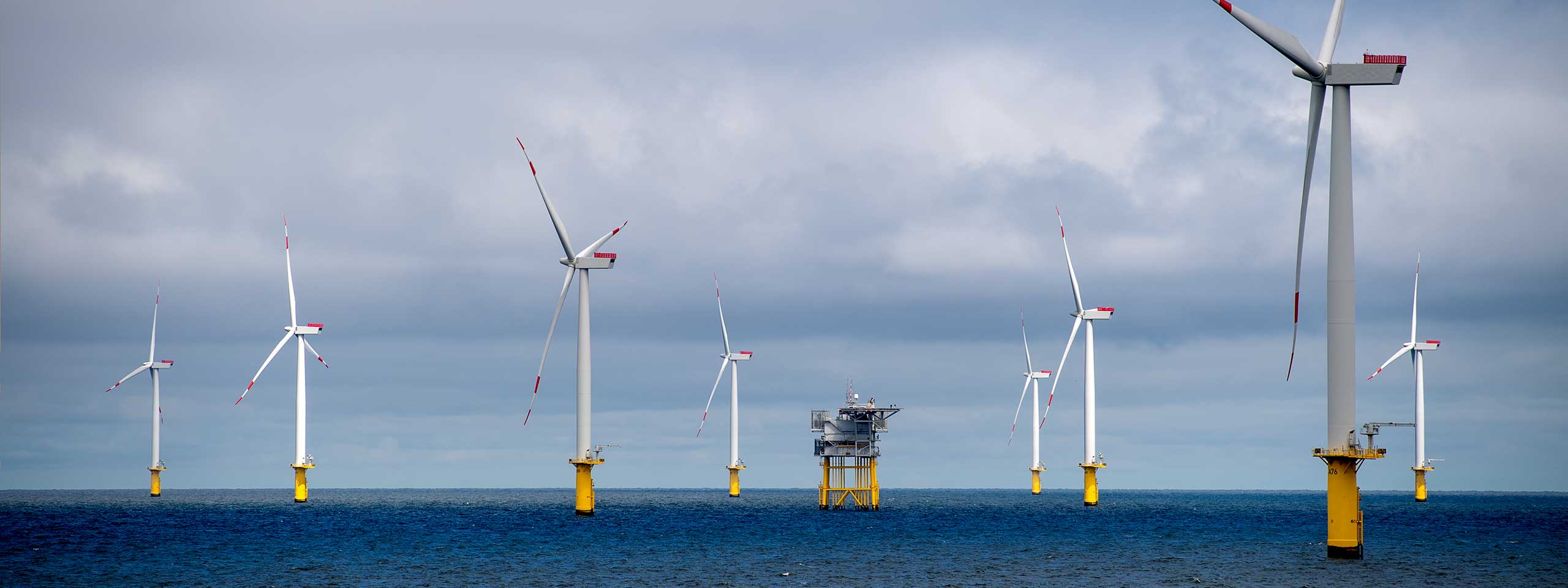 Windkraftanlagen im Meer mit gelben Fundamenten und grauem Himmel im Hintergrund.
