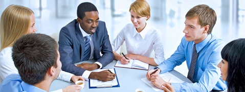 Eine Gruppe von Personen um einen Tisch, die an einem Meeting teilnehmen und Notizen machen.