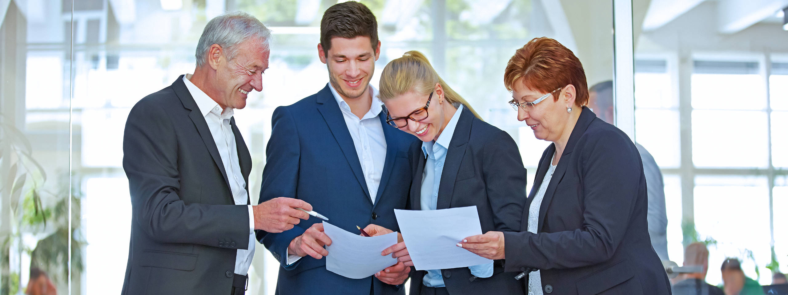 Fünf Personen in Businesskleidung, die Dokumente in einem modernen Büro besprechen.