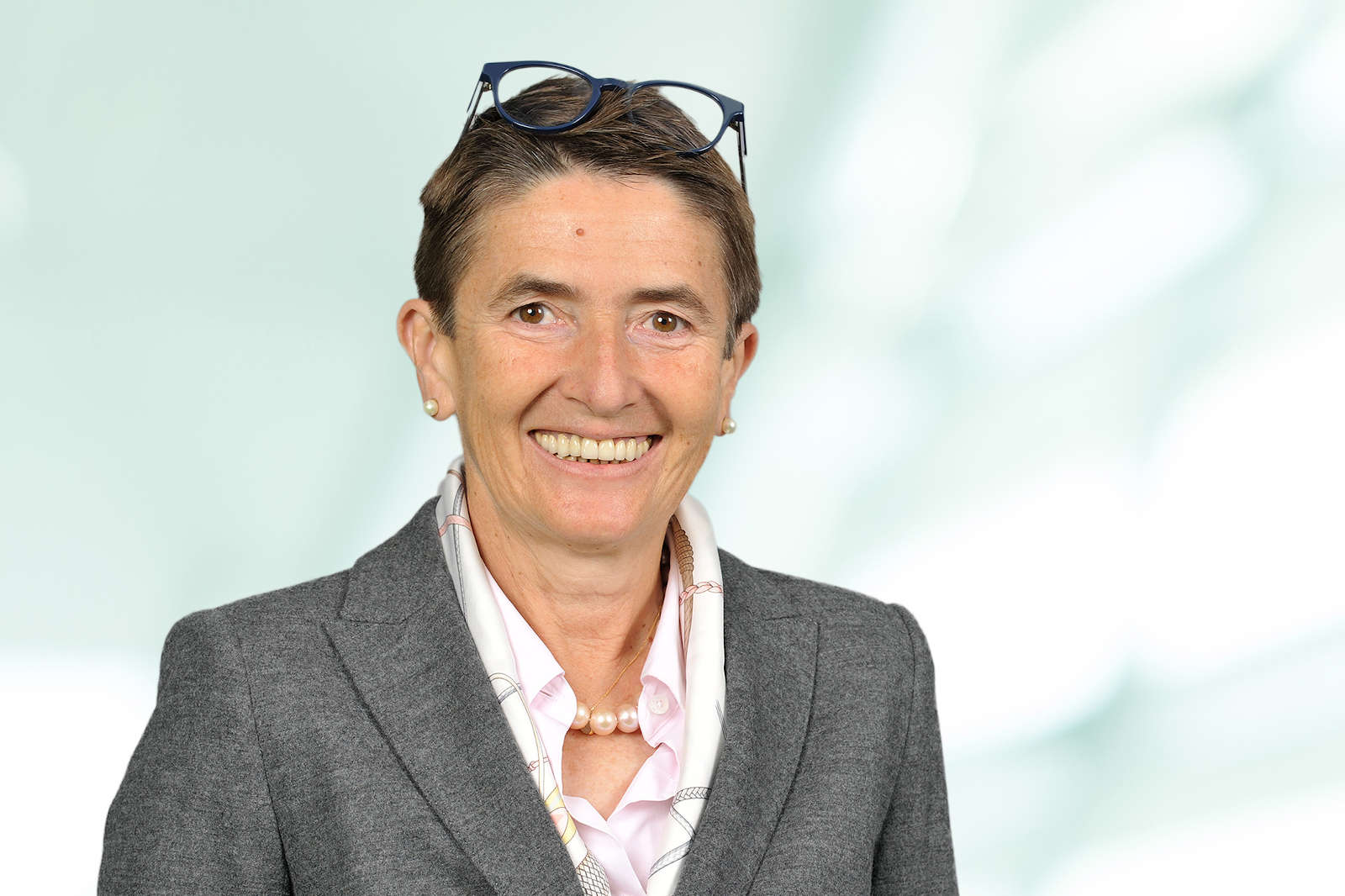 Eine Person in einem grauen Blazer und einer hellen Bluse mit Perlenkette. Im Hintergrund ist eine unscharfe, helle Fläche. Portrait von Zvezdana Seeger.