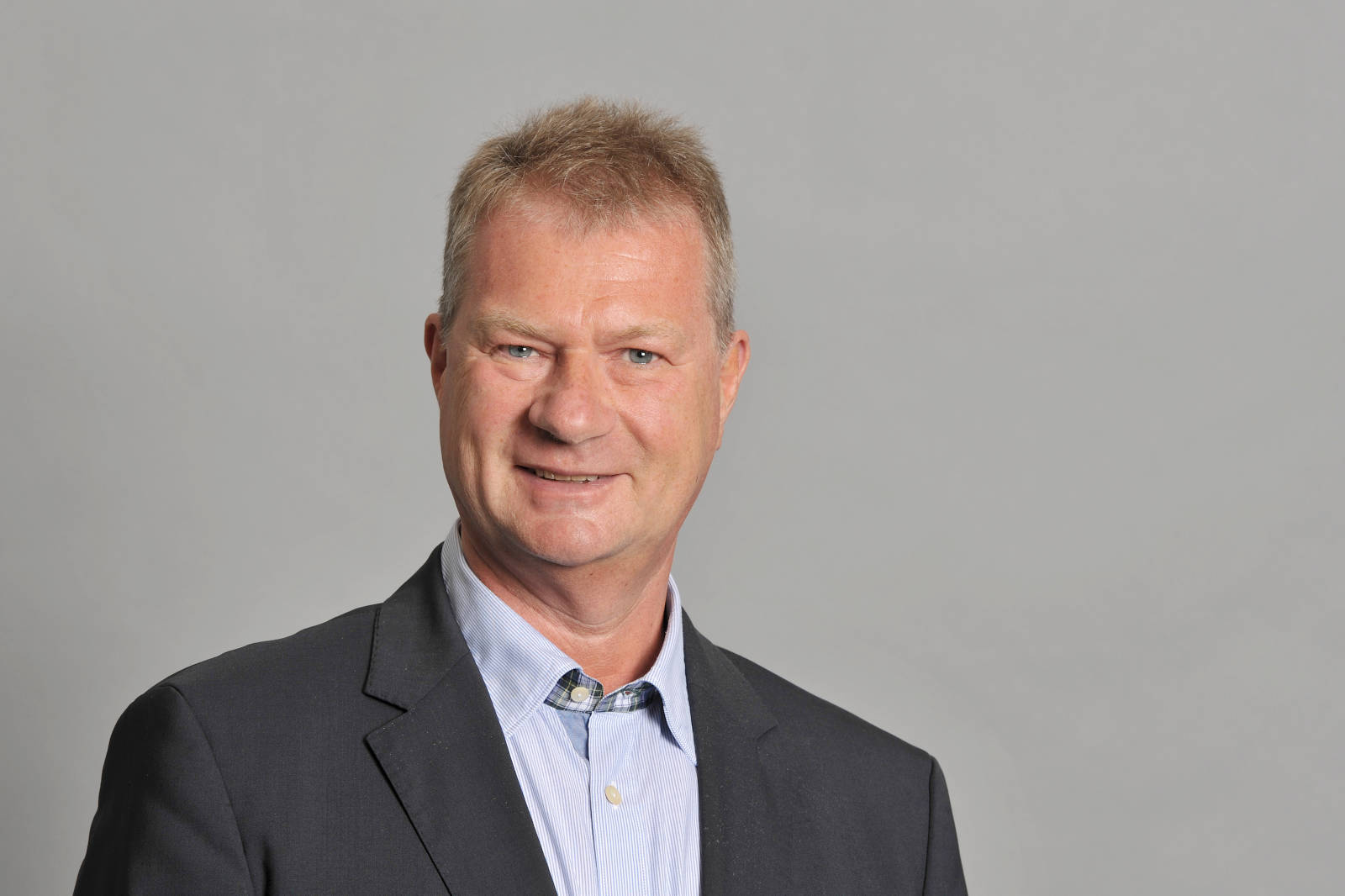 A man in a suit stands against a plain grey background, captured in a professional photo setting. Portrait of Dr. Hans Bünting.