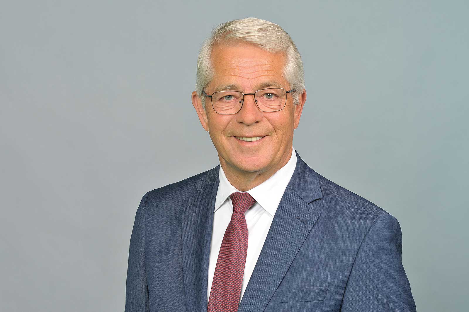 Ein professionell gekleideter Mann steht an einem Geländer in einer modernen Umgebung. Portrait von Dr. Stefan Schulte.