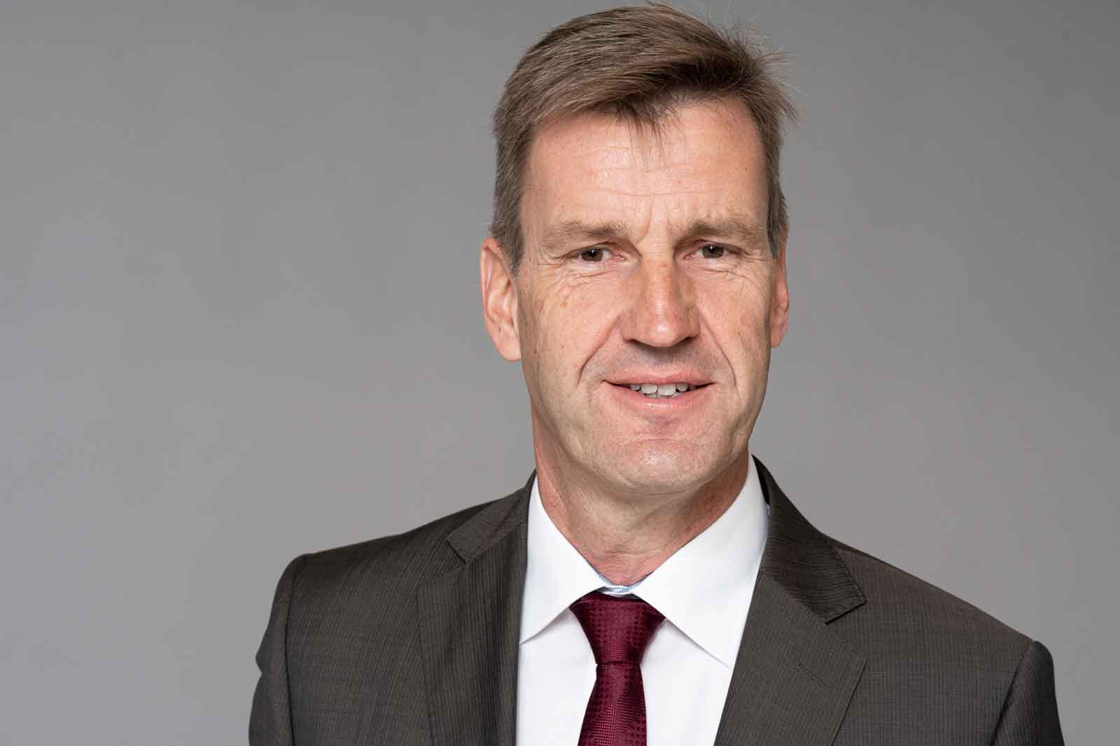 A man in a grey suit with a red tie poses against a neutral background. Portrait of Dr. Andreas Wagner.