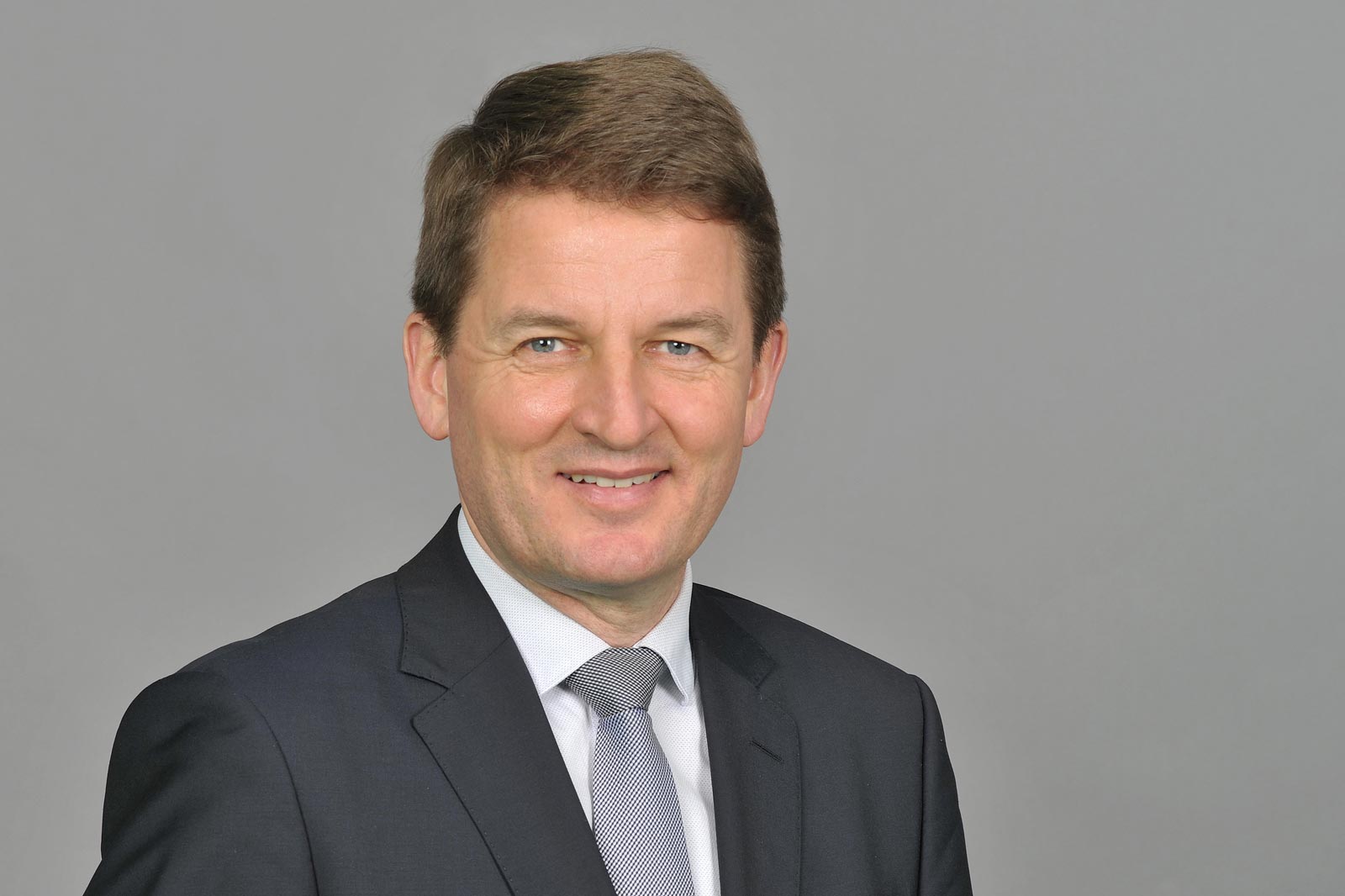A man in a suit with a blue shirt and tie against a grey background. Portrait of Prof. Jörg Rocholl, PhD.
