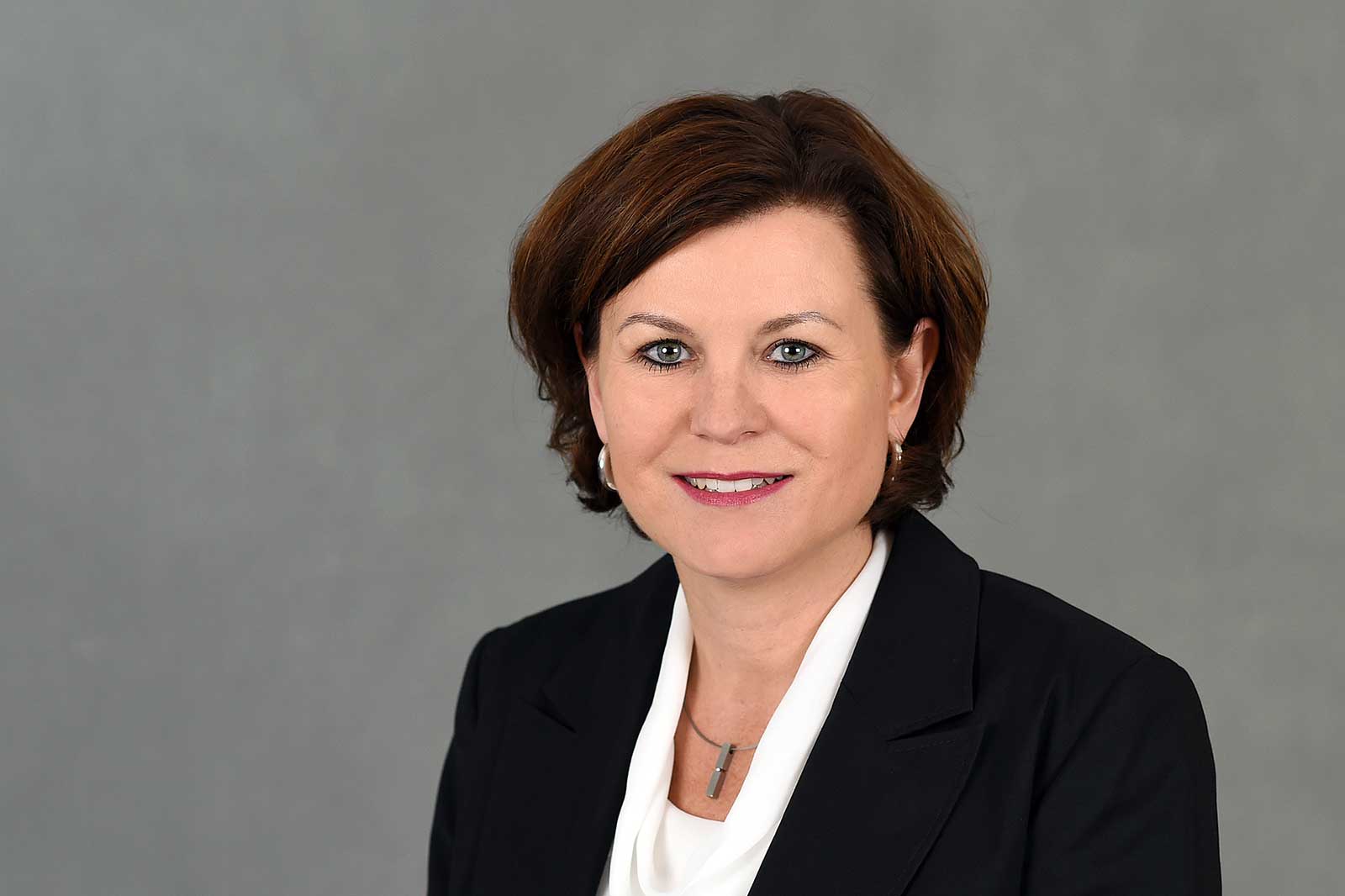 A person is wearing a black blazer and a white blouse. The background is grey. Portrait of Marion Weckes.