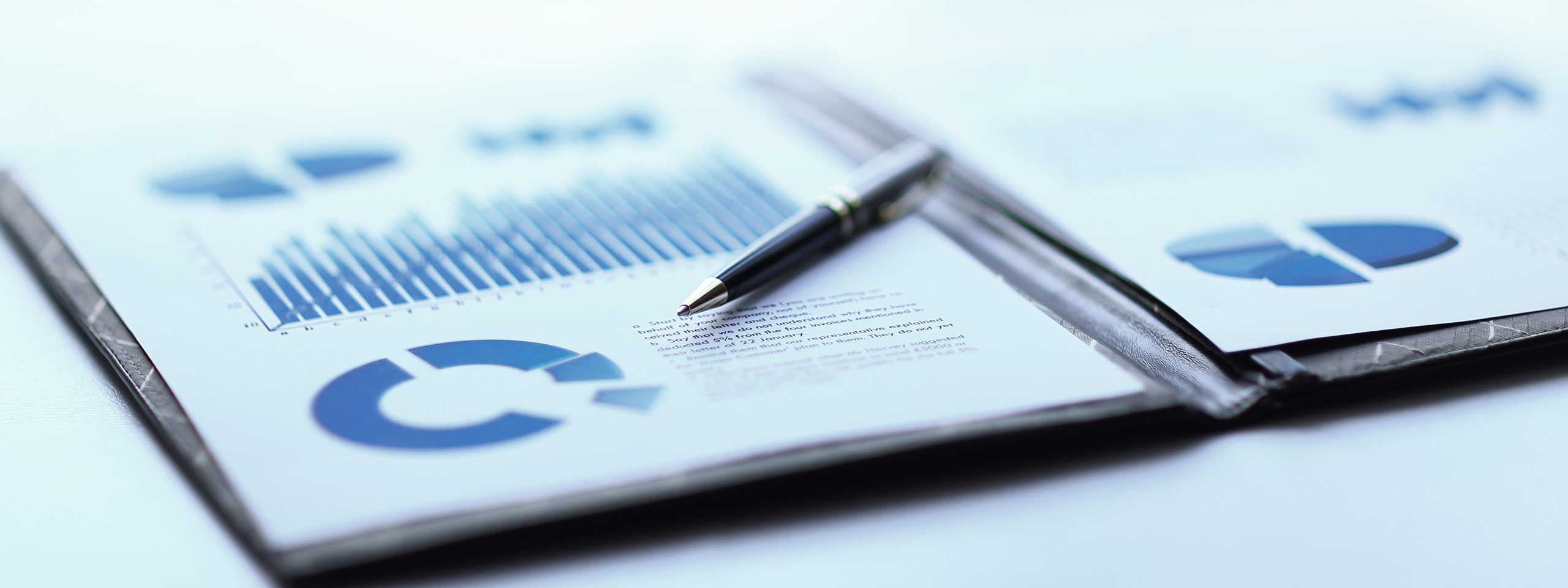 Grafiken und Diagramme auf einem Blatt Papier liegen neben einem Stift auf einem Schreibtisch.