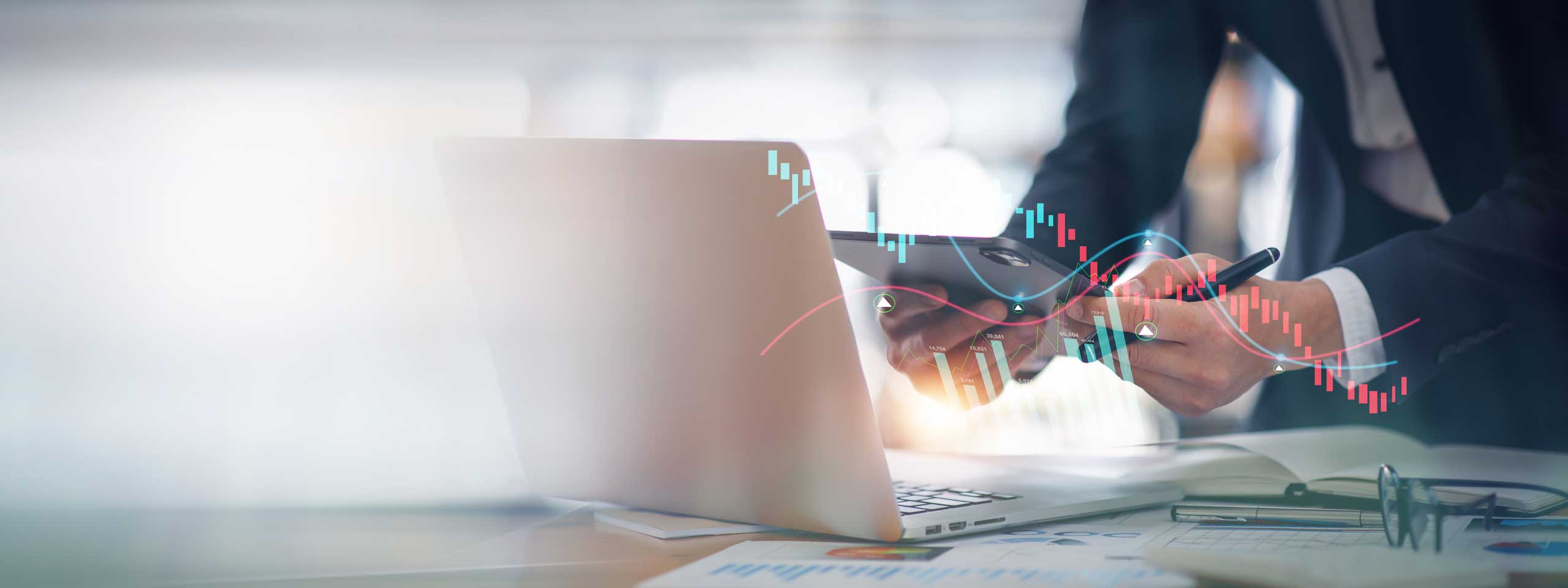 Eine Geschäftsperson arbeitet an einem Laptop und analysiert Finanzdaten auf einem Tablet.