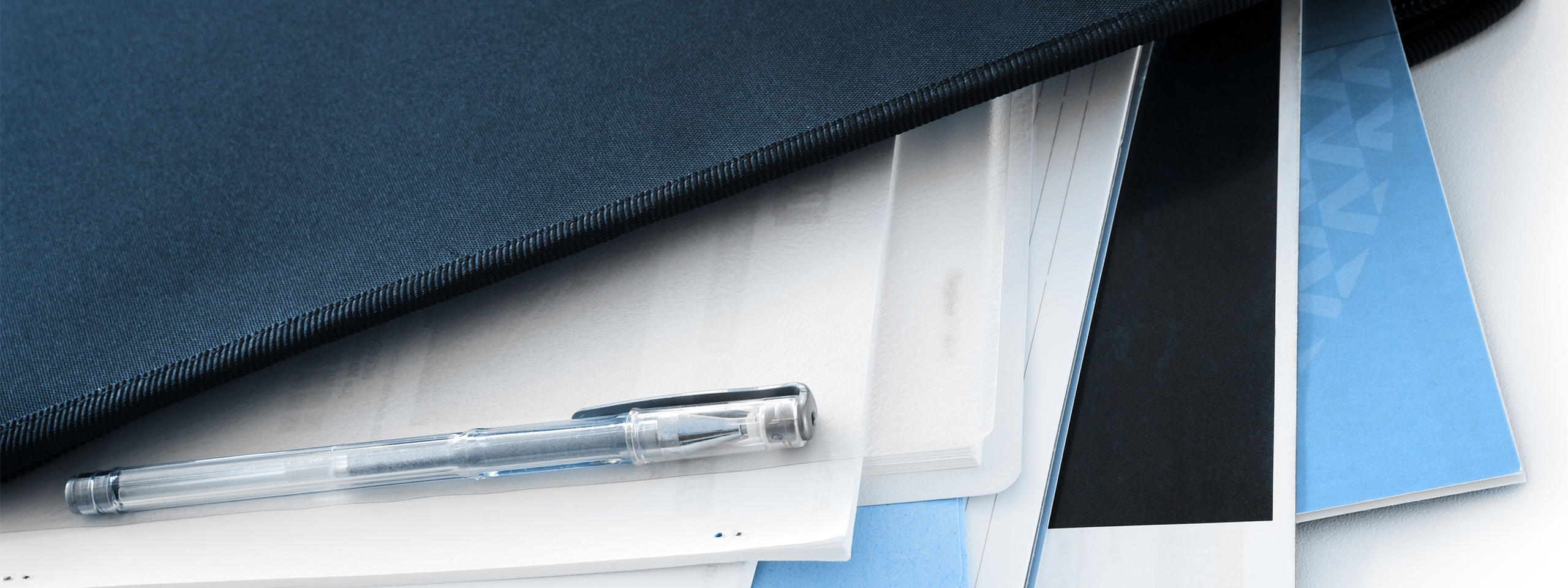 A black folder with several sheets of paper and a transparent ballpoint pen rests on a light table.