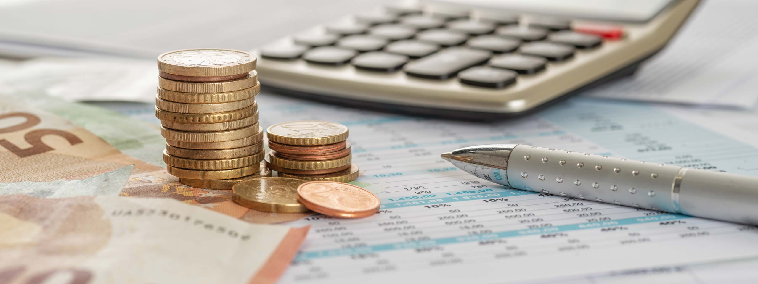 A stack of coins and banknotes on a financial document next to a calculator and a silver pen.