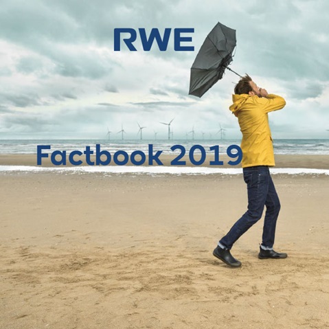 A person in a yellow raincoat holds an umbrella on the beach, with wind turbines visible in the background.