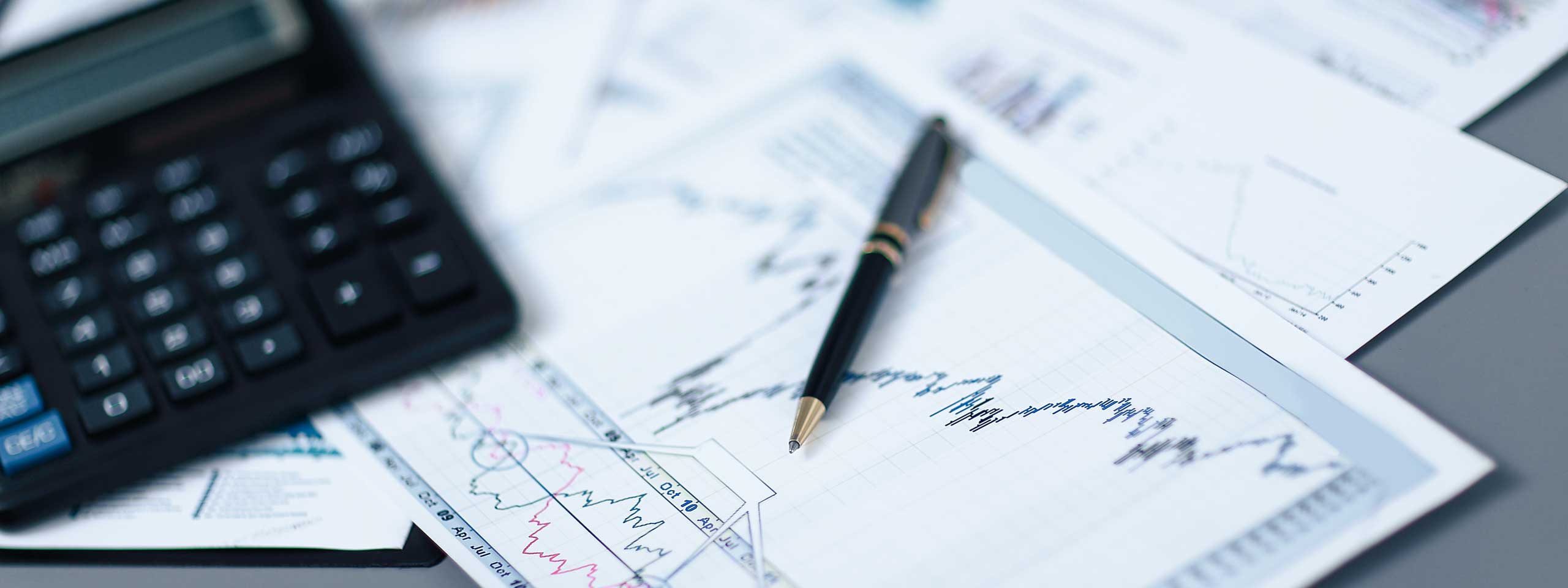 Ein Taschenrechner, ein schwarzer Stift und Finanzdokumente mit Diagrammen liegen auf einer grauen Oberfläche.