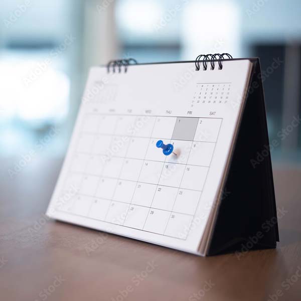 A desk calendar with a blue push pin marking a specific date is placed on a table.