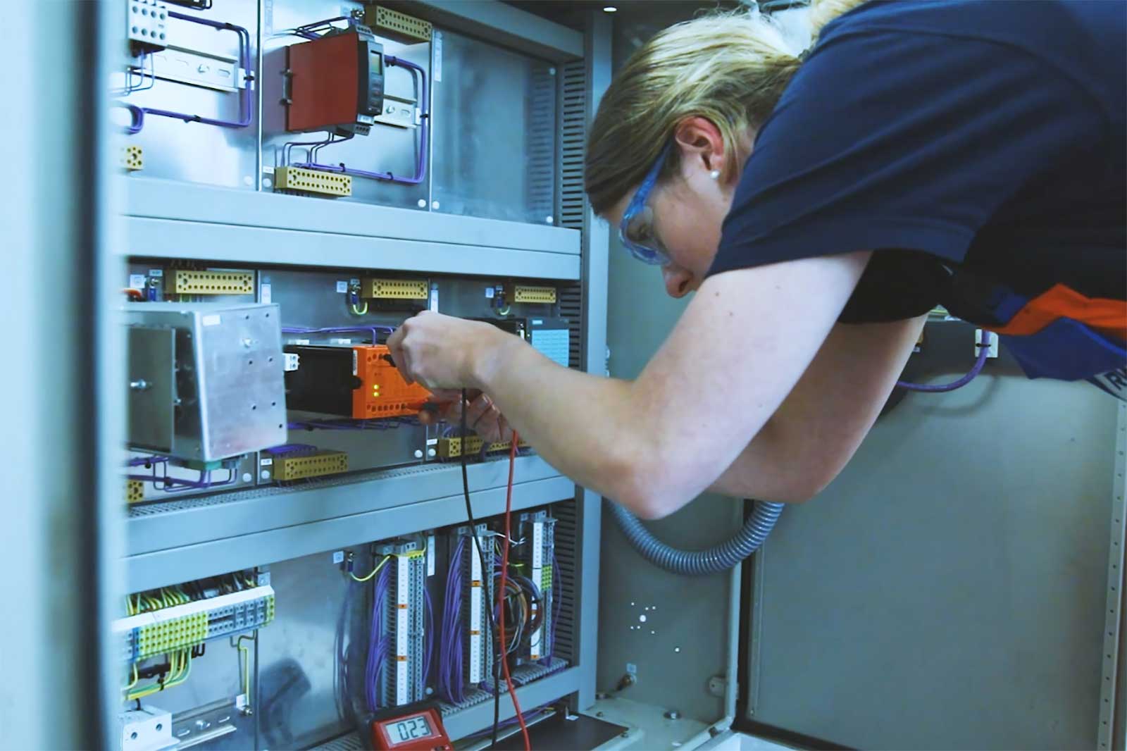 Eine Elektronikerin für Automatisierungstechnik arbeitet an einem Sicherungskasten.