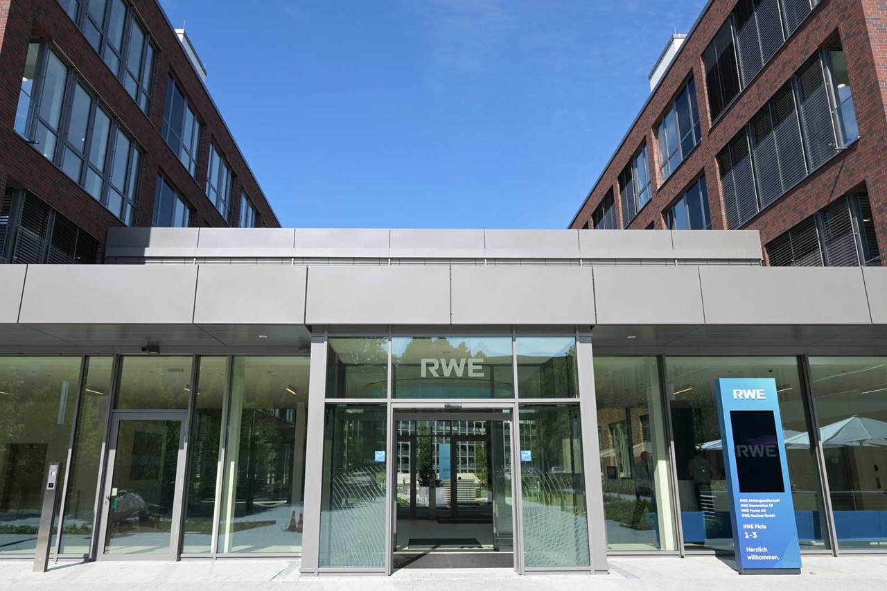 Moderne Eingangsfront eines RWE-Gebäudes mit großen Fenstern und Informationssäule im Freien.