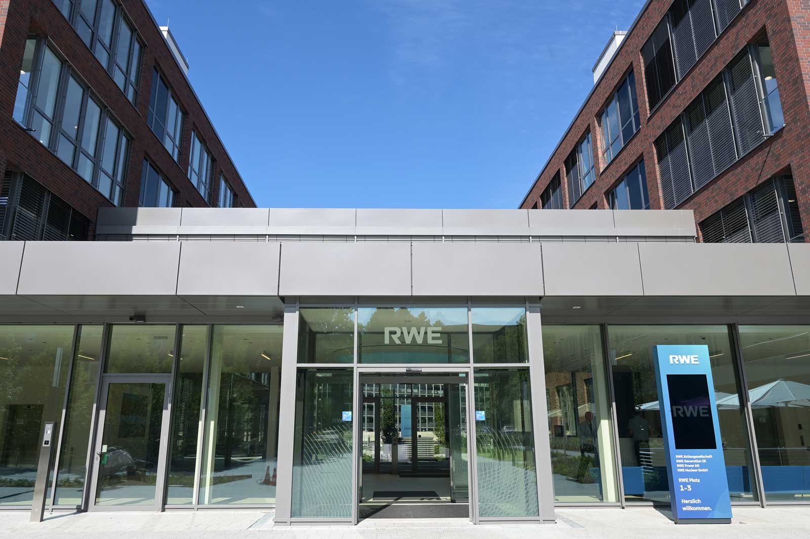 Modern entrance facade of an RWE building featuring large windows and an outdoor information stand.