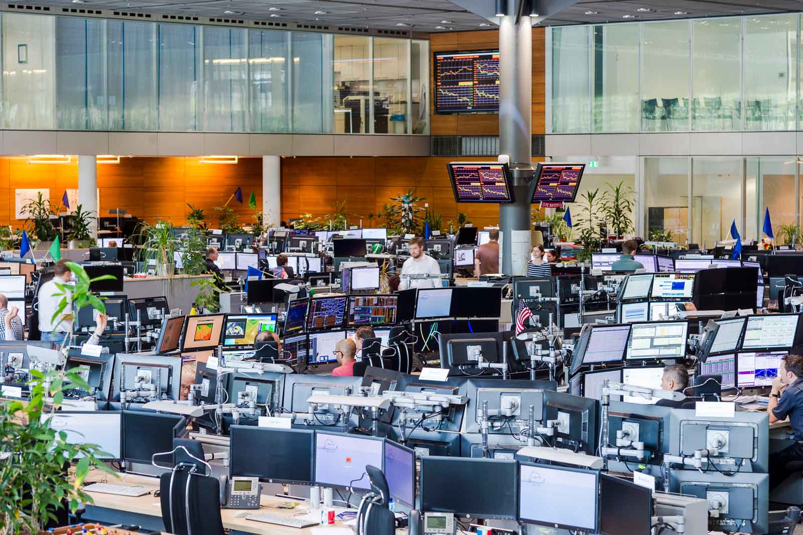 A modern office filled with workstations and screens, where employees are actively working. Plants add to the pleasant atmosphere.