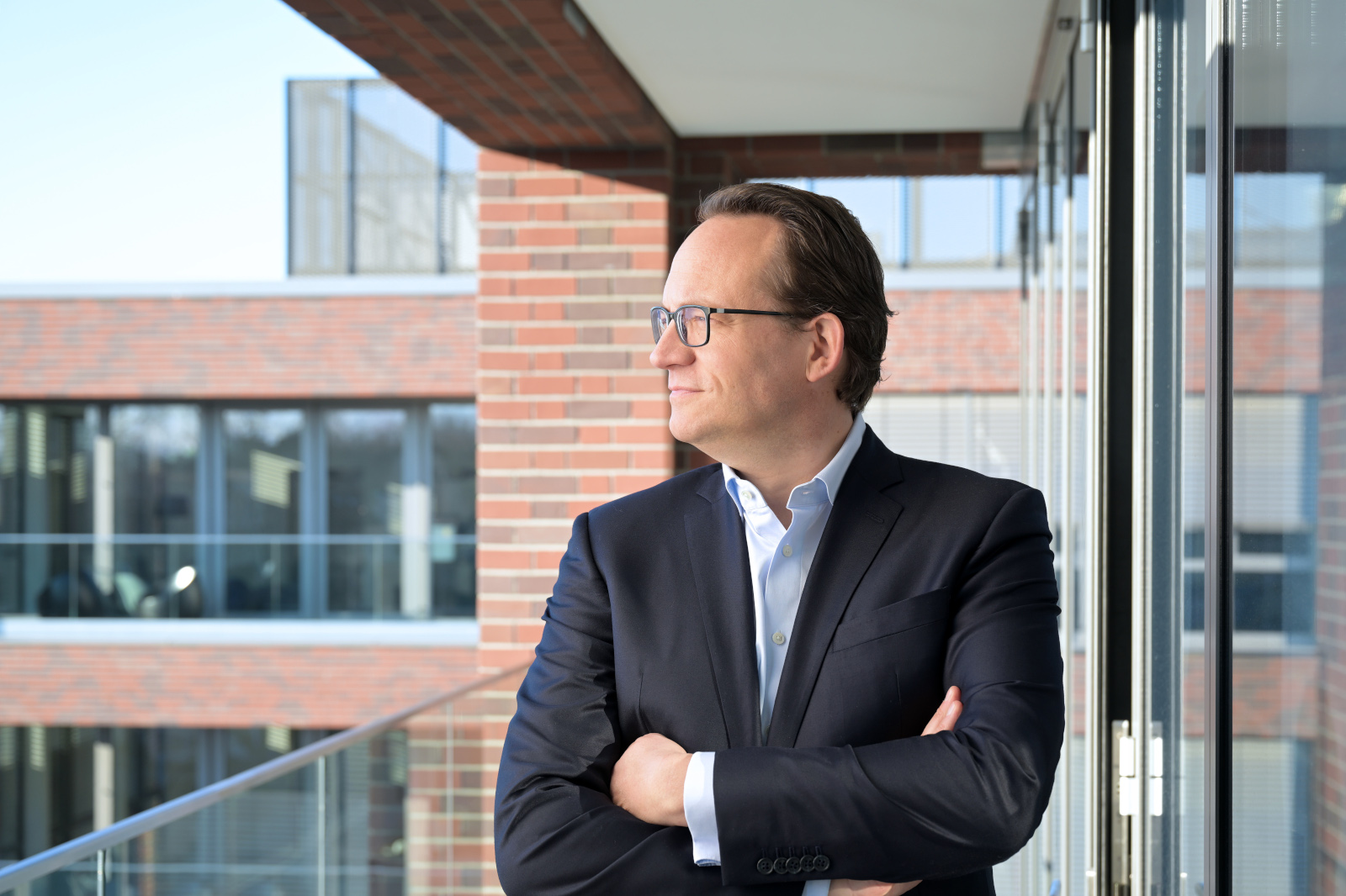 Ein Mann in einem Sakko schaut von einem Balkon aus in die Ferne.