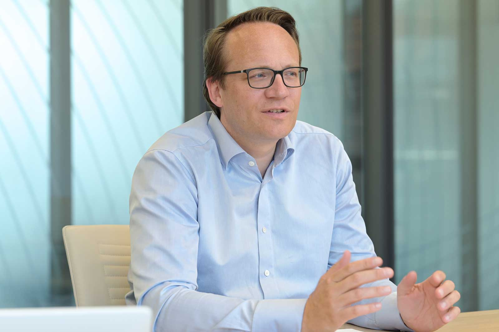 A person in a light blue shirt gestures during a meeting in a modern office setting.