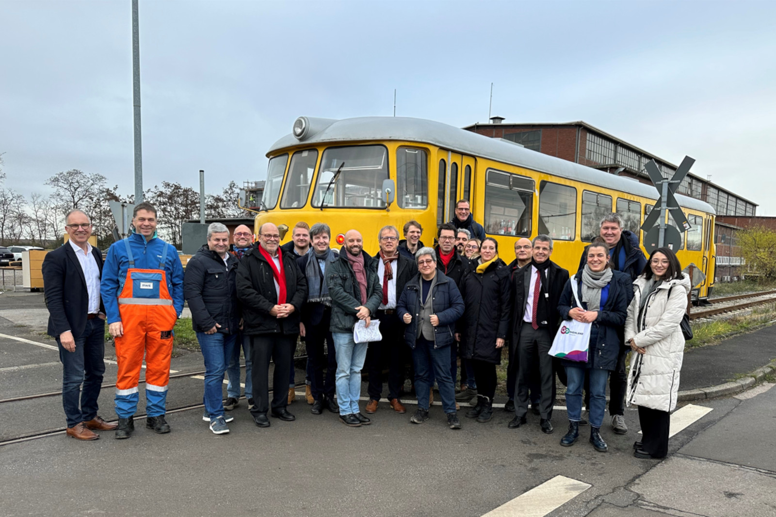 Eine Gruppe von Personen posiert vor einem gelben Zug an einem Bahnübergang.