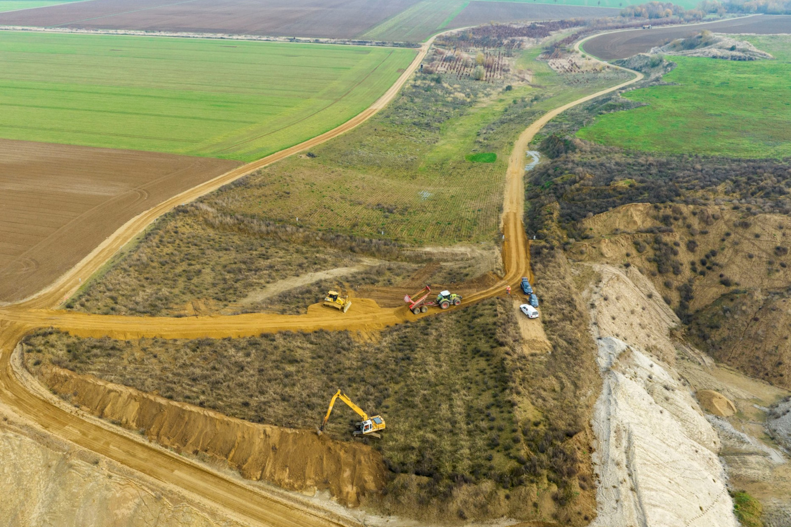 Eine Luftaufnahme einer Baustelle mit Maschinen auf Schotterwegen, umgeben von Ackerland und Hügeln.