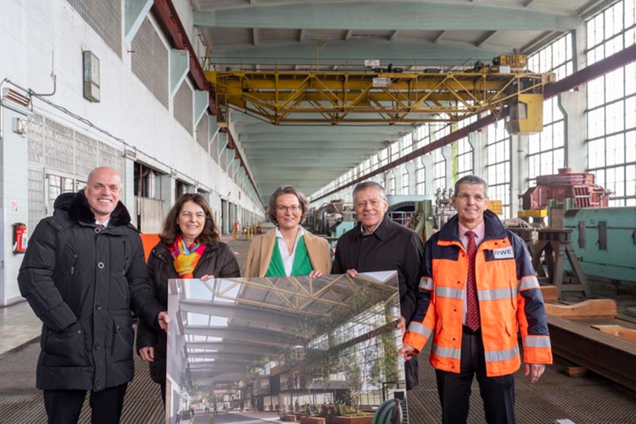 Gruppe von Personen, die einen großen architektonischen Druck in einem Industriegebäude mit hohen Fenstern im Hintergrund halten.