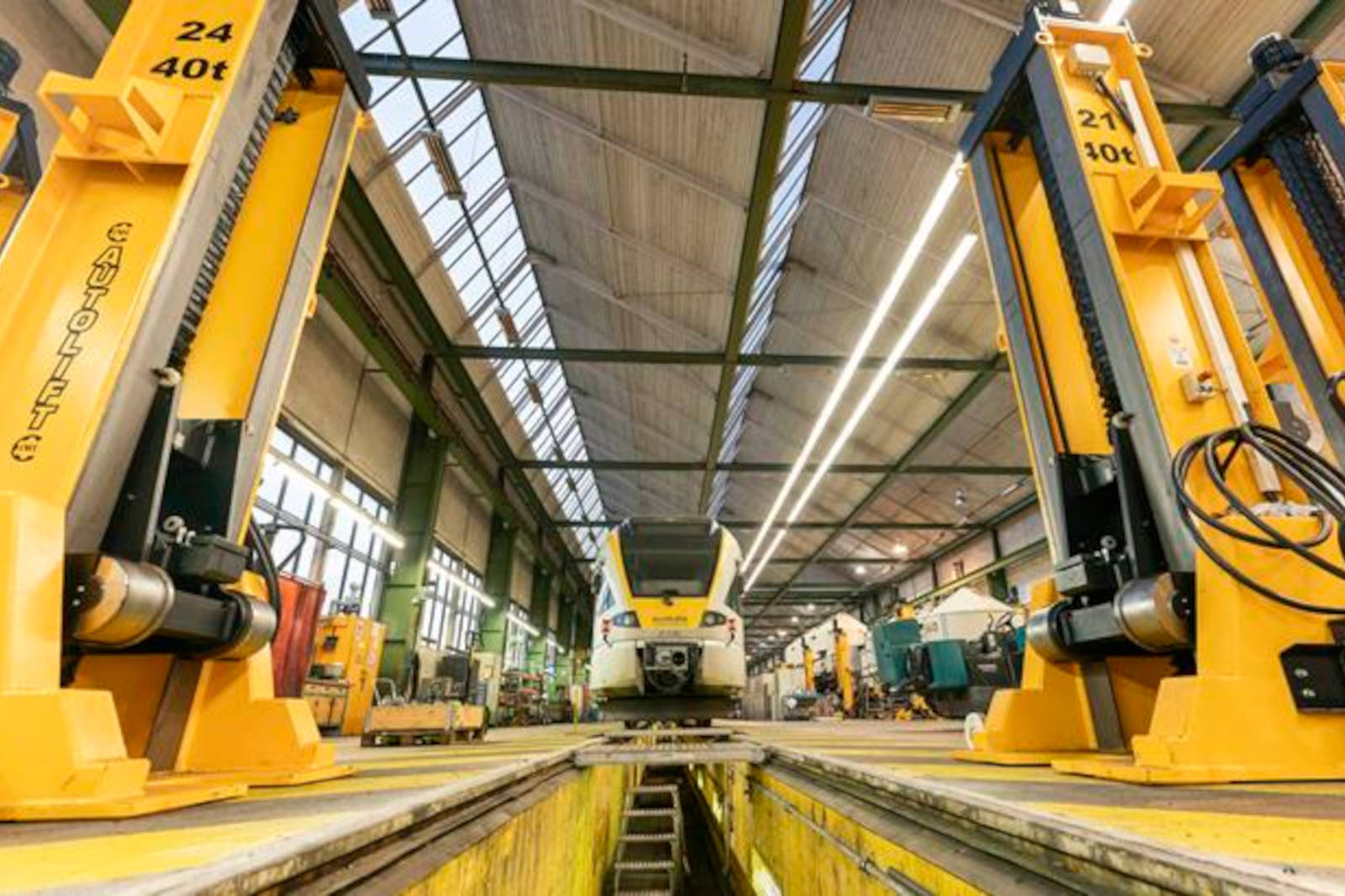 Eine geräumige Werkstatt mit zwei gelben Hebebühnen, die ein Fahrzeug über einem Graben halten, umgeben von verschiedenen Werkzeugen.