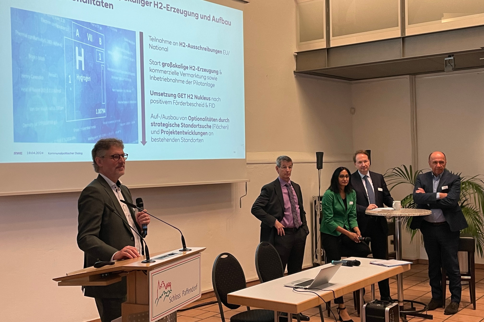 Eine Präsentation zur Wasserstoffproduktion findet mit Rednern und Publikum in einem Konferenzraum statt.