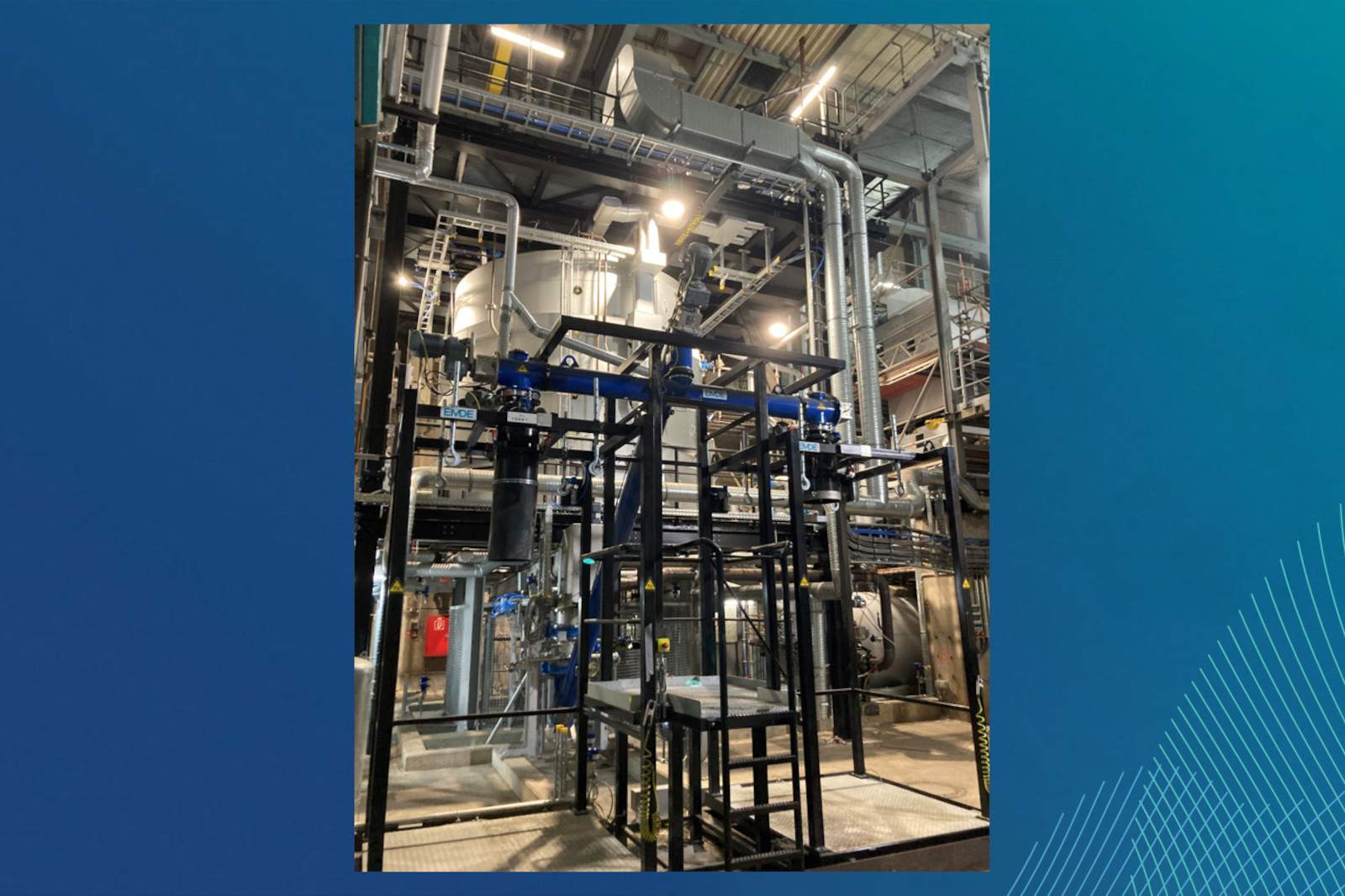 Industriemaschinen mit komplexen Rohrleitungen und einem großen Tank, beleuchtet in einer Produktionsstätte.