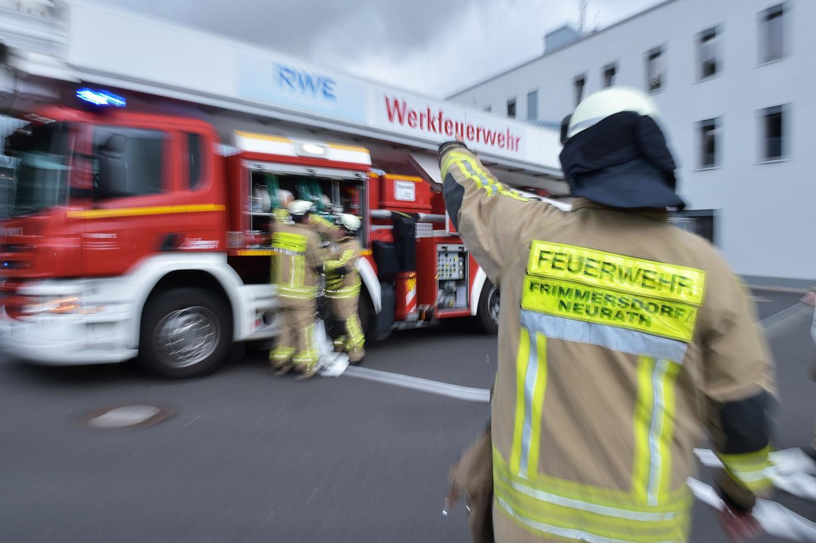 Ein Feuerwehrmann in Uniform weist Teams in der Nähe eines Löschfahrzeugs an. Die Szene ist geschäftig und actionreich.