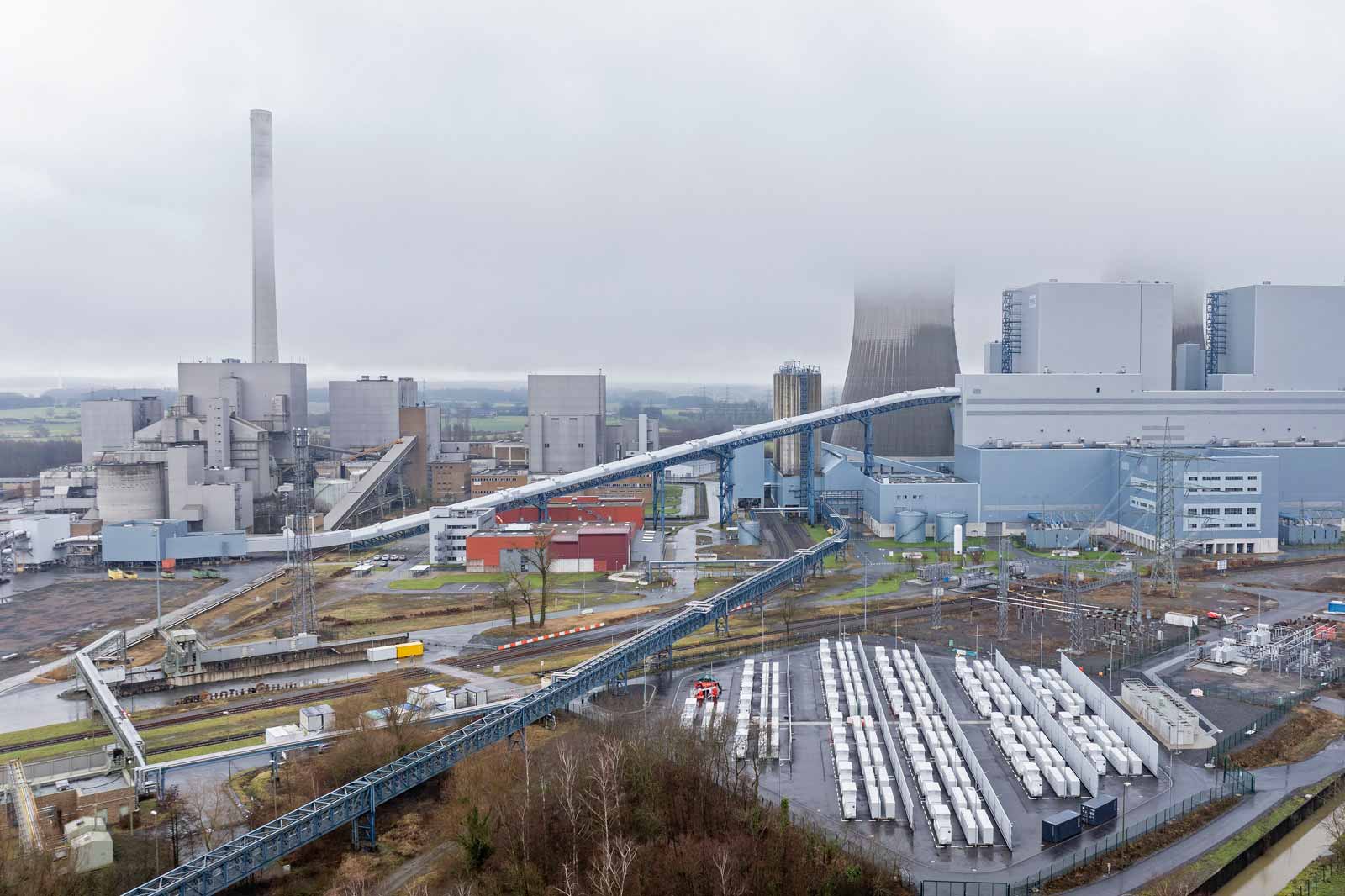 Eine große Industrieanlage mit einem hohen Schornstein, Förderbändern und verschiedenen Gebäuden unter bewölktem Himmel.